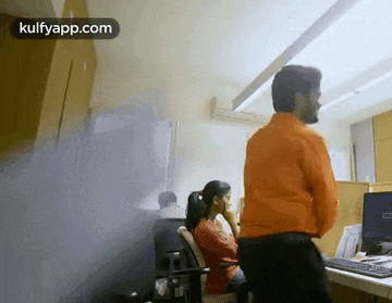 a man in an orange shirt is standing next to a woman in an office .