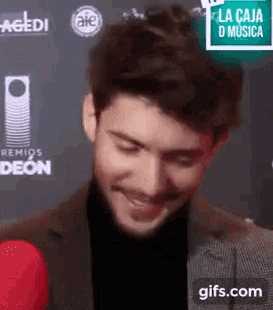 a man in a suit and black turtleneck is smiling and looking at the camera .