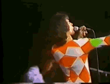 a woman singing into a microphone while wearing a colorful outfit