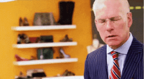 a man in a suit and tie is standing in front of a shelf full of shoes .