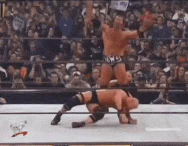 two men are wrestling in a wrestling ring while a crowd watches .