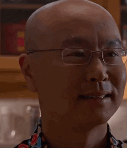a bald man wearing glasses and a colorful shirt looks at the camera