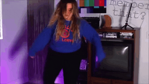 a woman in a blue sweater is dancing in front of a television and a sign that says member that