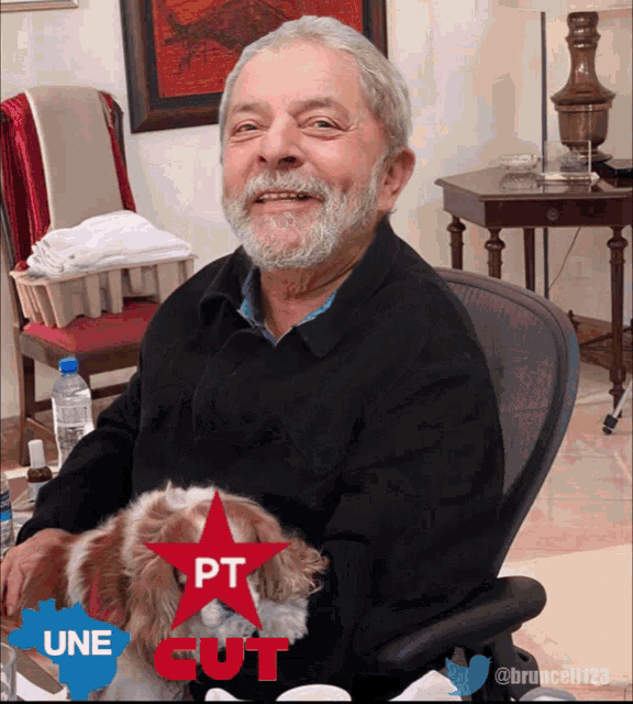 a man with a beard is sitting in a chair holding a small dog with a red star that says pt on it