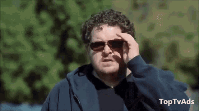 a man wearing sunglasses and a blue hoodie has toptvads written on the bottom right