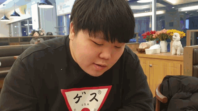 a man wearing a black guess sweatshirt sits in a restaurant