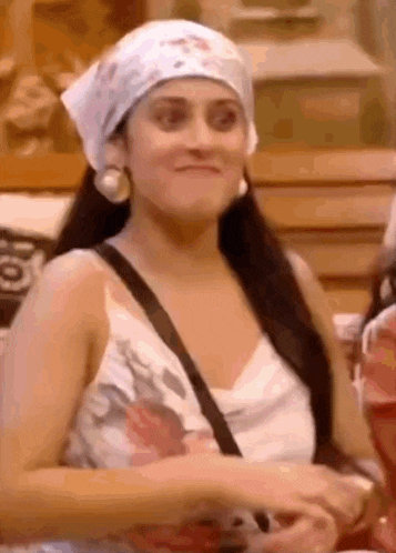 a woman wearing a head scarf and a white tank top is making a funny face .