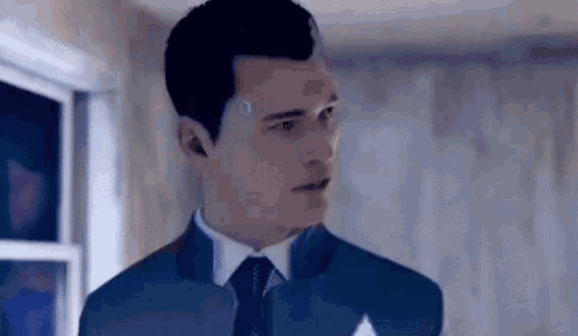 a man in a suit and tie is standing in a room and looking at the camera .