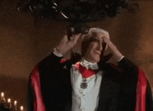 a man in a tuxedo and a red cape is holding his head .