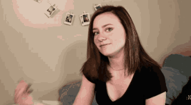a woman in a black shirt is sitting in front of a wall with pictures hanging from it