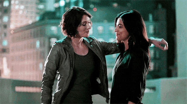 two women are standing next to each other on a rooftop and hugging .