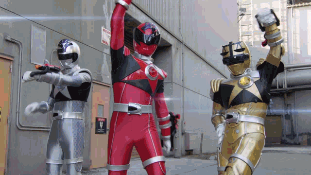 three power rangers are standing in front of a building with one wearing a red suit