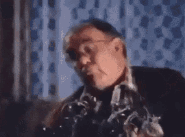 a man with glasses is sitting on a couch in front of a window looking through a microscope .