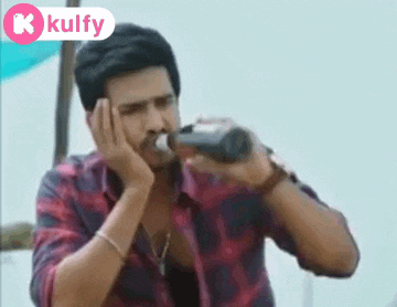 a man in a plaid shirt is drinking from a bottle with his hand on his face .