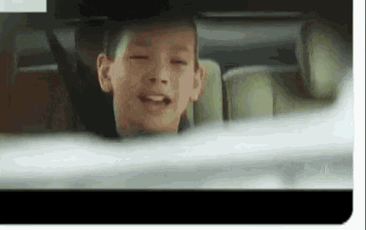 a young boy sitting in the back seat of a car with his eyes closed .