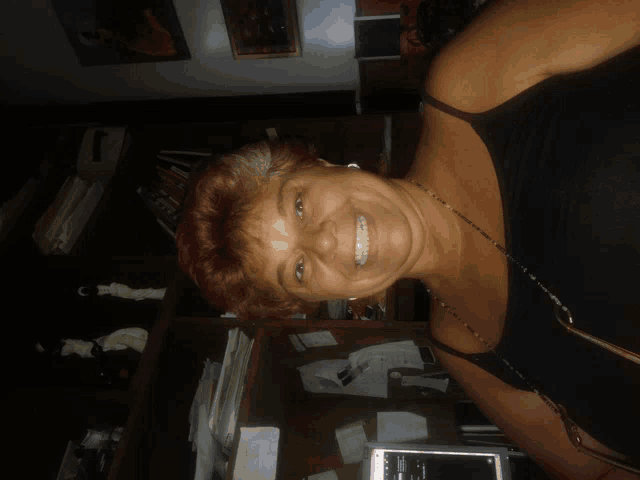 a woman in a black tank top is smiling in front of a laptop