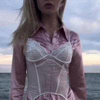 a woman in a pink shirt and white corset is standing on the beach