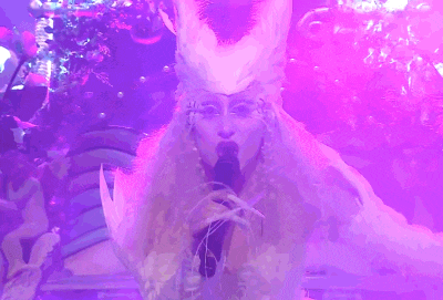 a woman in a white fur coat singing into a microphone in a purple light