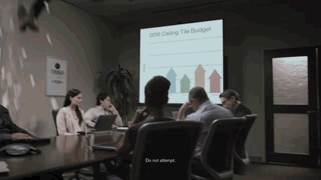 a group of people in a conference room looking at a projector screen which says 2016 ceiling tile budget