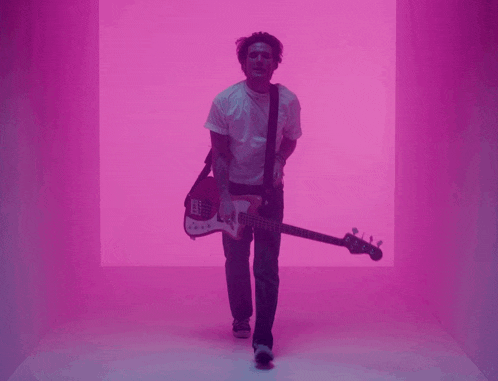 a man in a white shirt is holding a guitar in a pink room