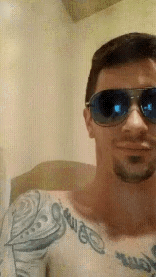 a shirtless man wearing sunglasses has a tattoo on his arm that says ' swag '