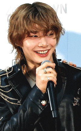 a man in a leather jacket is smiling while holding a microphone in front of a sign that says vn