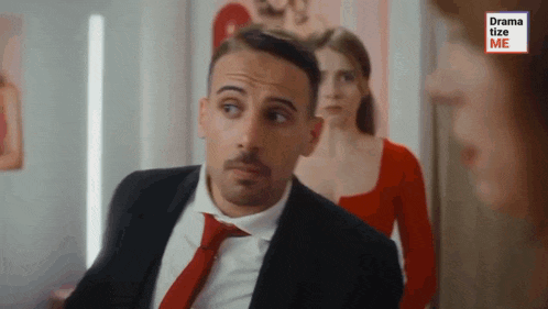 a man in a suit and tie is looking at a woman in a red dress