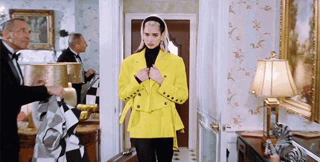 a woman in a yellow jacket is walking down a hallway