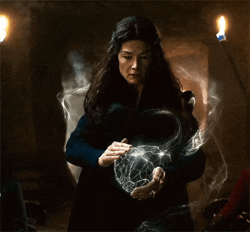 a woman in a blue dress is holding a sphere in her hands in a dark room .