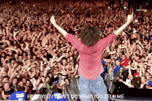 a man in a pink shirt stands in front of a crowd and says " fuck you i wan 't do what you tell me