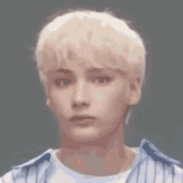 a close up of a young man with blonde hair wearing a blue striped shirt .