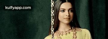 a woman wearing a yellow dress and a gold necklace is standing in front of a black curtain .