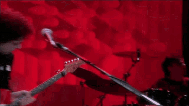 a man is playing a red guitar in front of a red wall