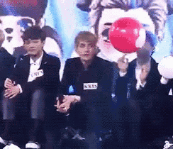 a man with a name tag that says kks is holding a red balloon in front of a group of people
