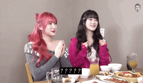 two girls are sitting at a table with plates of food and a sign that says ' ? '