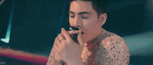 a man in a sequined shirt is drinking from a glass with zky written on the bottom