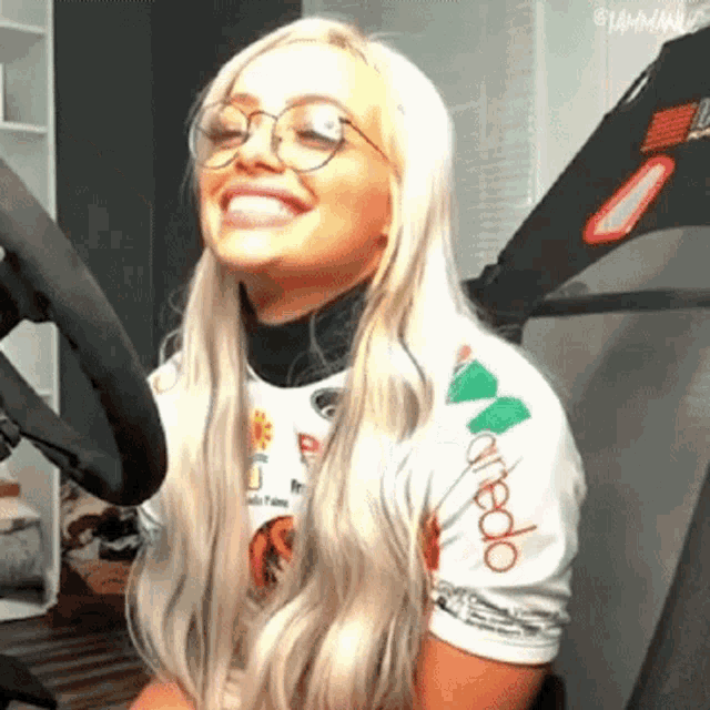 a blonde woman wearing glasses and a white shirt is smiling in front of a microphone .