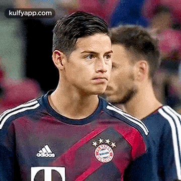 a soccer player wearing a purple and red adidas jersey is standing next to another player .