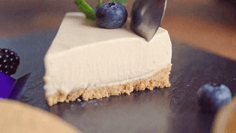 a piece of cheesecake with a blueberry on top is being cut with a knife .