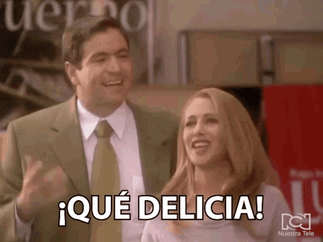 a man in a suit and tie stands next to a woman who is smiling and says " que delicia "