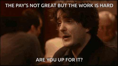 a man sitting at a table with the words " the pay 's not great but the work is hard " above him