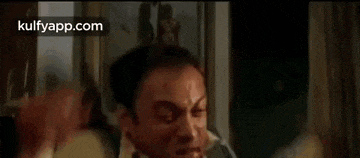 a man is laying on a bed with a knife in his mouth and another man is standing next to him .