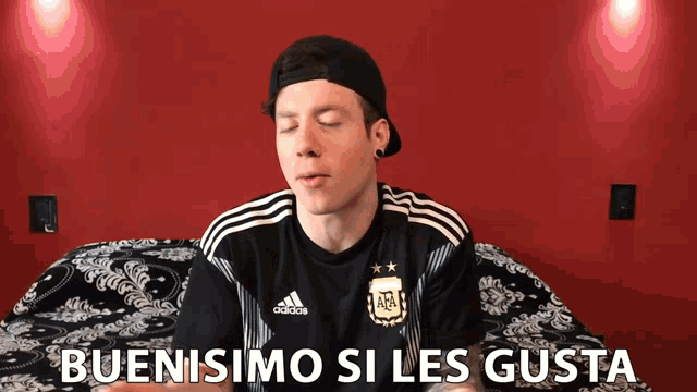 a man wearing a black adidas shirt is sitting on a bed
