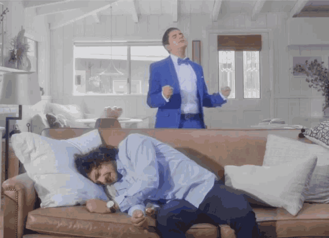 a man in a tuxedo is dancing while another man lays on a couch