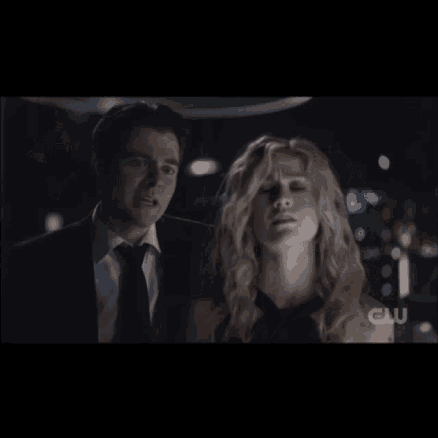 a man in a suit and tie is talking to a woman in a dark room
