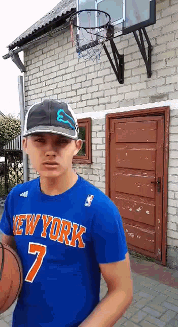 a man wearing a new york shirt is holding a basketball in front of a brick building