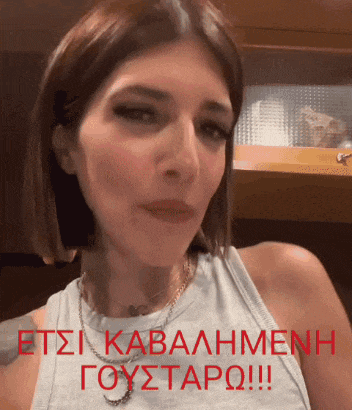 a woman wearing a white tank top with a necklace and the words " etsi kabalmenh goystaro !!! " in red