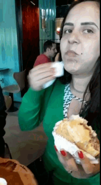 a woman in a green sweater is eating a hamburger