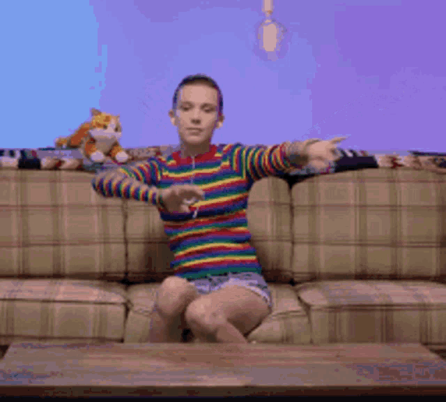 a woman in a rainbow striped shirt is sitting on a couch
