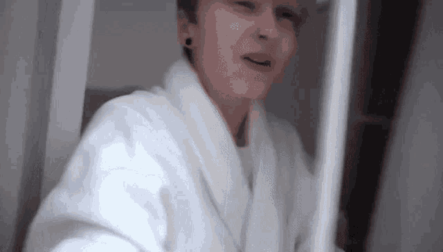 a man in a white robe is standing in front of a mirror in a bathroom .